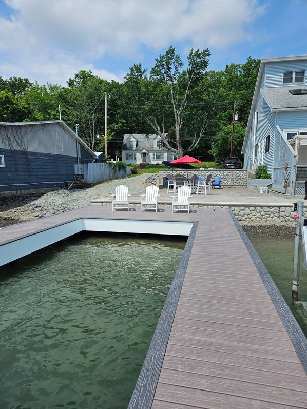 A dock leading to a small pool with white chairs and a red umbrella.