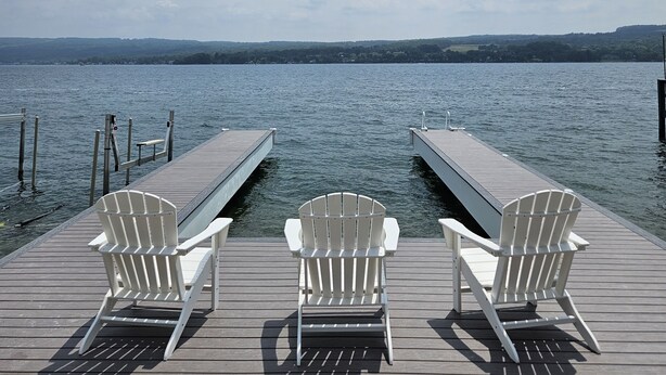 Un muelle de madera con tres sillas Adirondack blancas mirando a un lago tranquilo.