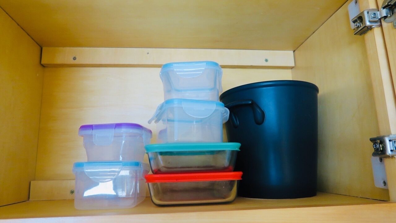 Un meuble en bois contenant des récipients en plastique transparent et un pot noir.