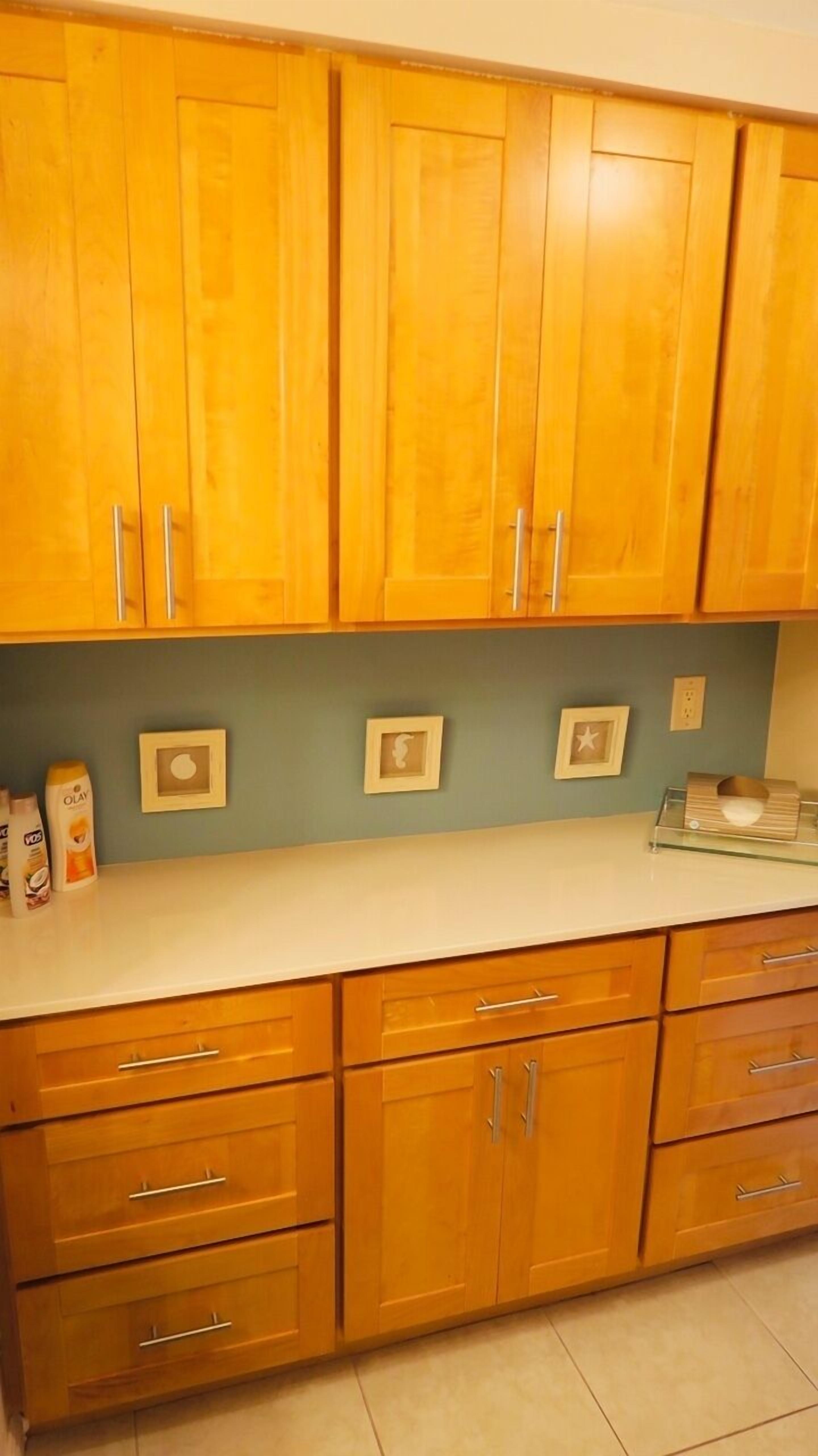 A kitchen with wooden cabinets, a white countertop, and three framed pictures on the wall.