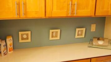 A kitchen with wooden cabinets, a white countertop, and three framed pictures on the wall.