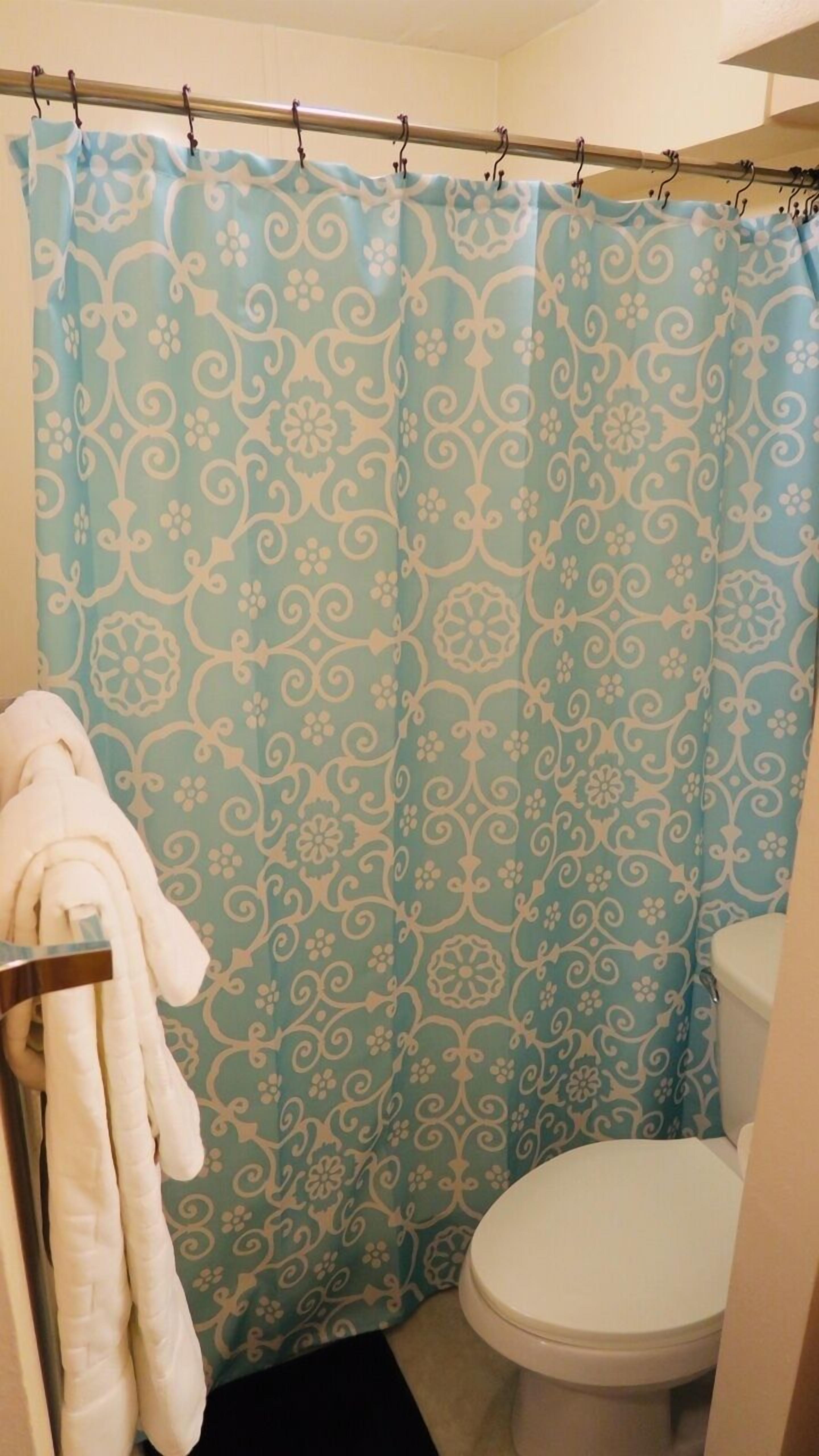 A bathroom with a shower curtain featuring a floral pattern, a white toilet, and a towel rack with a white towel.