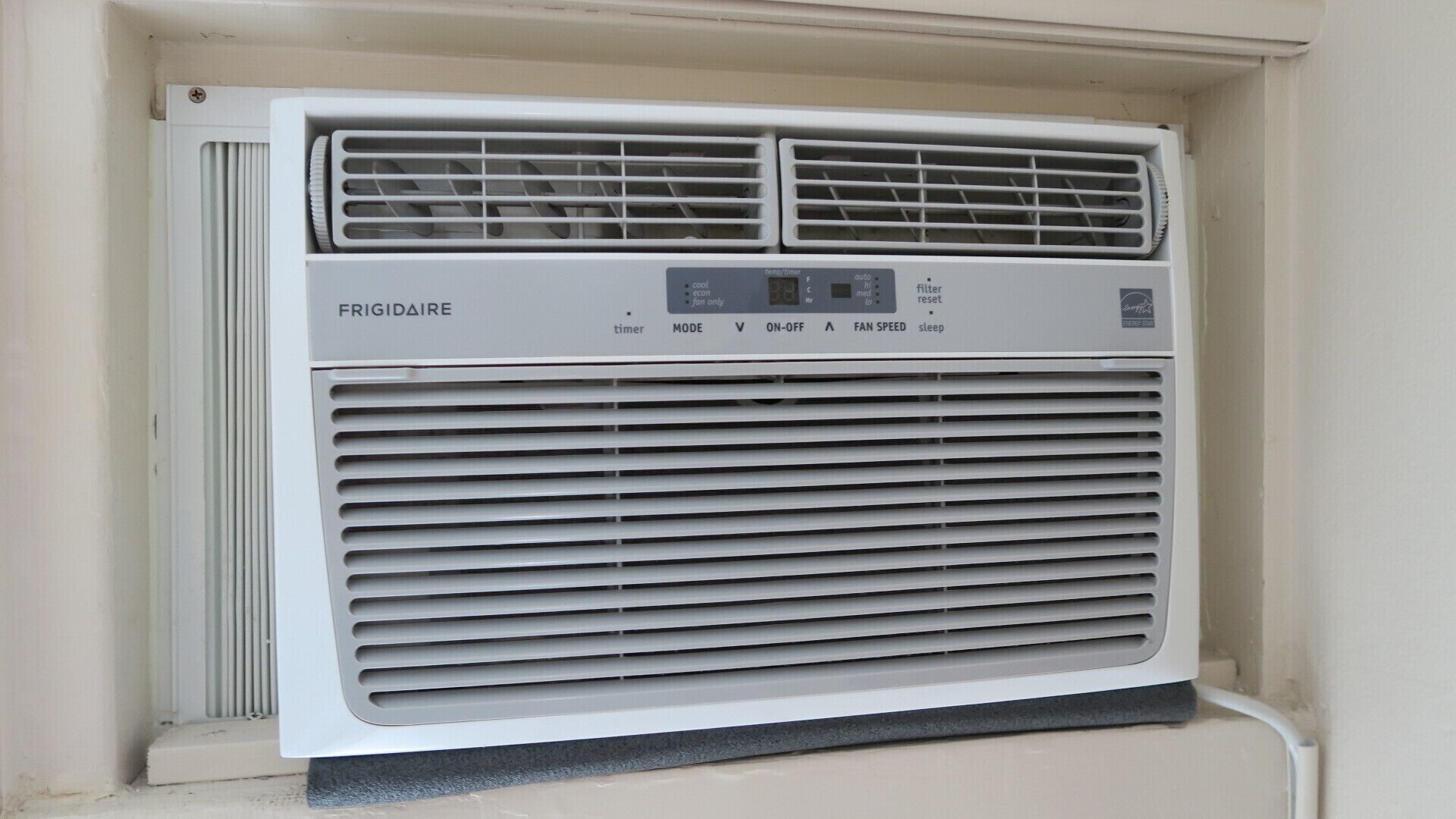 A white air conditioner unit with a control panel labeled "FRIGIDAIRE" and buttons for "timer," "mode," "on-off," "fan speed," and "sleep."