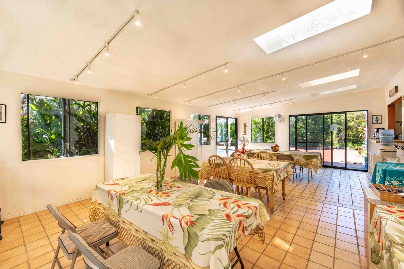 A spacious dining area with high ceilings, large windows, and a tropical theme.