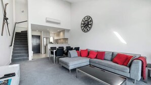 Un salon moderne avec un canapé d’angle gris, une table basse et un coin repas avec des chaises.