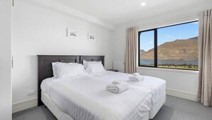 Une chambre d’hôtel avec un grand lit, deux tables de chevet, une fenêtre donnant sur la montagne et une lampe fixée au mur.