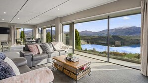 Ein geräumiges Wohnzimmer mit großem Fenster und malerischem Blick auf einen See und Berge.