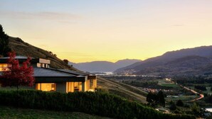 Ein modernes Haus mit Satteldach, gelegen an einem Hang mit Blick auf ein Tal und ferne Berge.