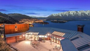 A modern building with a glass-roofed terrace overlooking a lake and mountains.
