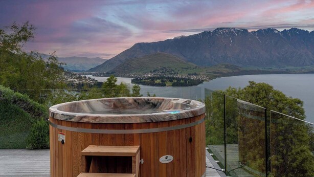 A wooden hot tub with a view of a lake and mountains.