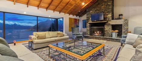 A cozy living room with a stone fireplace, a large window offering a mountain view, and a comfortable seating area.