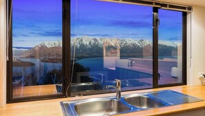 A kitchen with a large window offering a view of snow-capped mountains and a lake.
