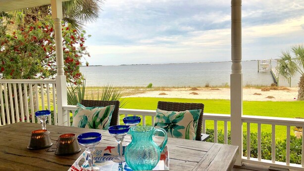 A wooden table with blue glassware and a tray, set on a porch with a view of the beach and ocean. - A Santa Rosa Sound Waterfront home on 2 acres with a private beach and 200’ dock (Mary Esther)