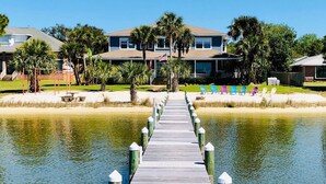 A wooden pier leading to a beachfront property with multiple-story buildings, palm trees, and a clear sky. - A Santa Rosa Sound Waterfront home on 2 acres with a private beach and 200’ dock (Mary Esther)
