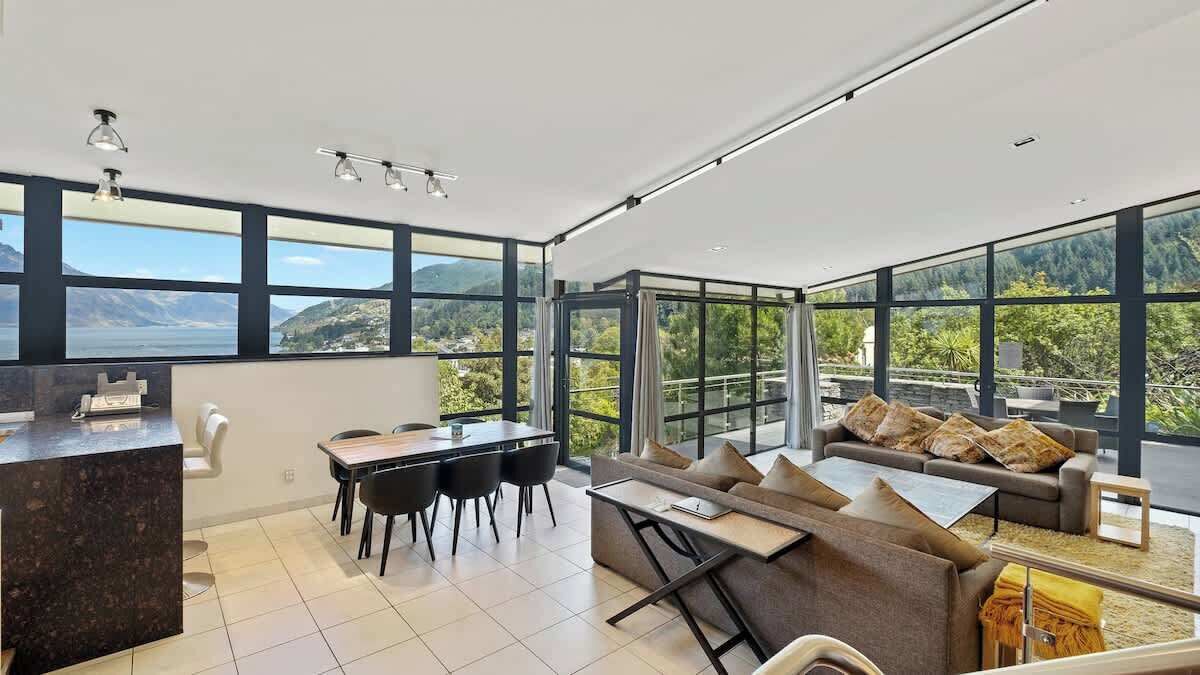 A modern interior with a dining area, sofa, and large windows offering a scenic view.