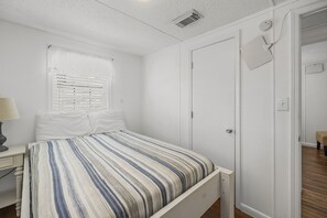 Un dormitorio con una cama, una mesita de noche, una ventana con persianas y una puerta.