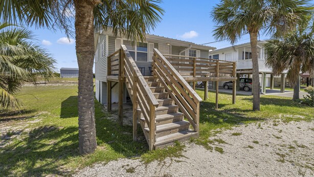A wooden staircase leading to a building with a balcony, surrounded by palm trees and a clear sky.