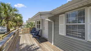 A wooden deck with outdoor seating, a palm tree, and a house with white siding and shutters.