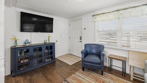 A living room with a dark blue cabinet, a television mounted on the wall, a blue leather chair, and a window with white blinds.