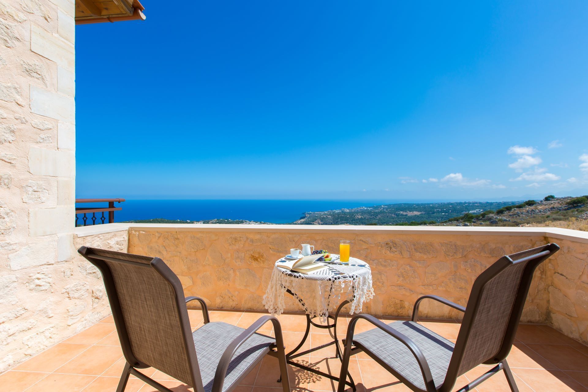 Un balcon avec deux chaises et une table, offrant une vue panoramique sur la mer et le paysage.