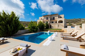 Un espace piscine avec des chaises longues, une piscine et un bâtiment en arrière-plan.