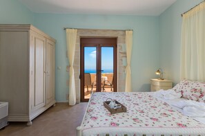 A bedroom with a bed, a wardrobe, a nightstand, and a view of the sea through a door. - Faethon, eco stone villa with private pool and sea view (Rethymno)