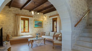 A cozy living room with a stone wall, wooden furniture, a painting, and a staircase. - Faethon, eco stone villa with private pool and sea view (Rethymno)