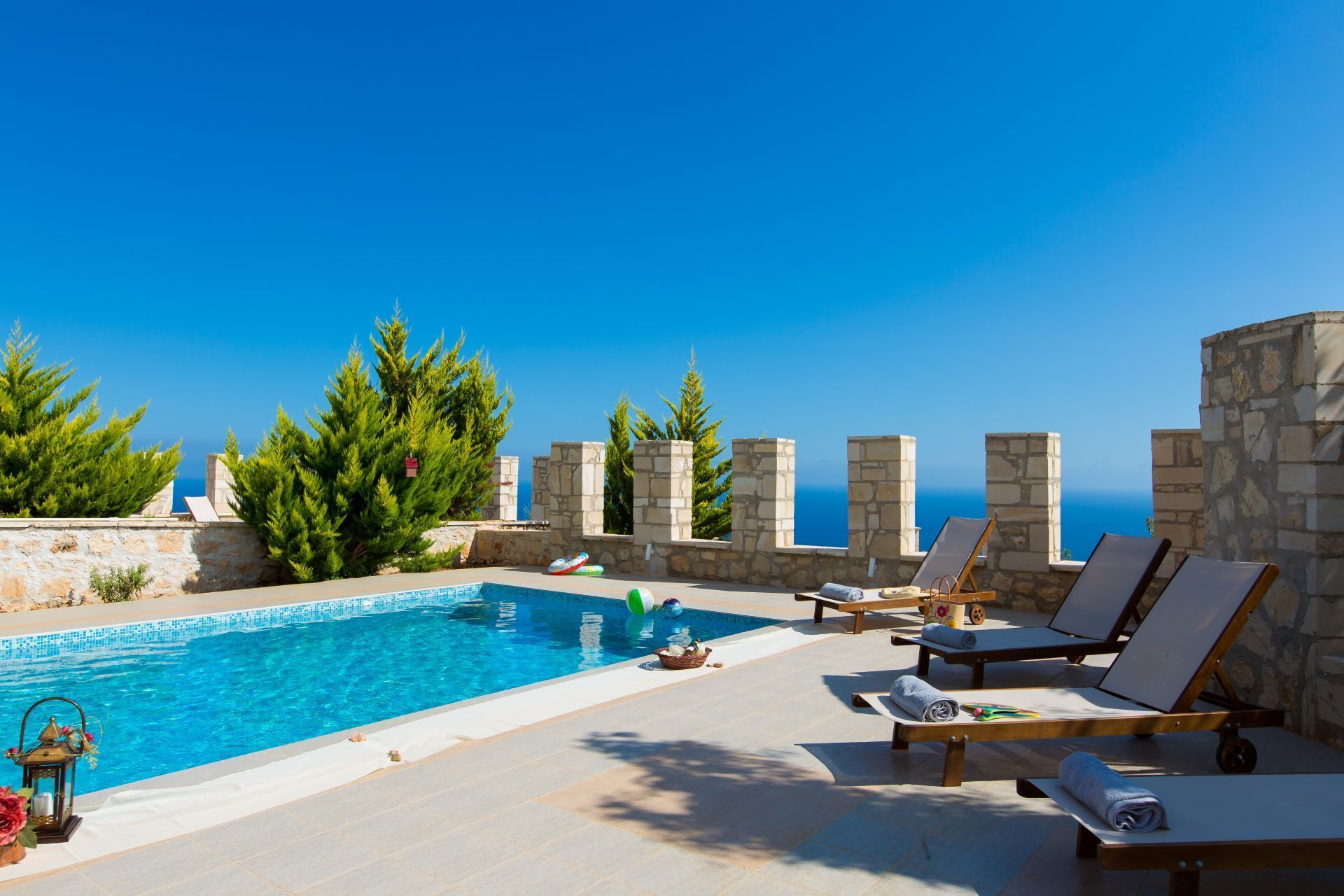 A poolside area with stone walls, lounge chairs, and a clear view of the sea.