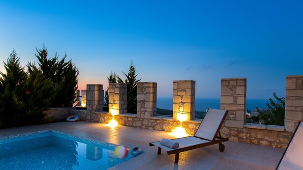 A poolside area with stone pillars, lounge chairs, and a view of the sea at dusk. - Faethon, eco stone villa with private pool and sea view (Rethymno)