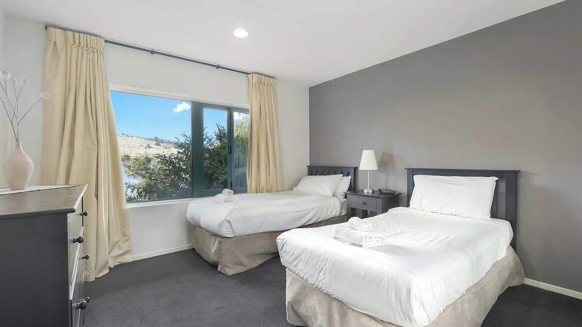 A hotel room with two beds, a desk, and a window with curtains.