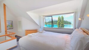 A bedroom with a large bed, a window with blinds, a wooden nightstand, and a framed picture on the wall.