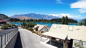 A residential area with a view of mountains and a lake. There are houses with sloped roofs and a paved road.