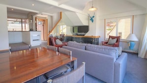 A spacious living area with a wooden dining table, grey sofas, and a TV.