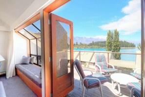 Ein Balkon mit einem Bett, Liegestühlen und Blick auf einen See und Berge.