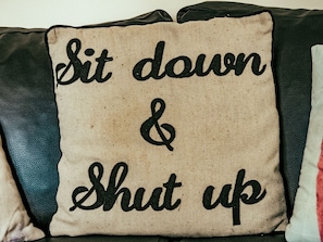 A pillow with the text "Sit down & Shut up".
