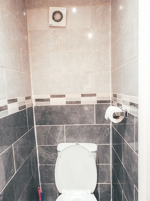 A bathroom with a toilet, a hand dryer, and a towel dispenser.