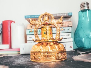 A golden decorative item with intricate designs, placed on a surface with books and a teal bottle in the background.