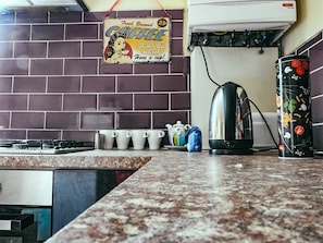 A kitchen with a brick backsplash, a coffee sign, a kettle, and a mug rack.