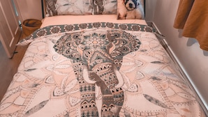 Ein Bett mit einer großen Bettdecke mit Elefantendesign, einem gemusterten Kissen und einer braunen Tagesdecke.