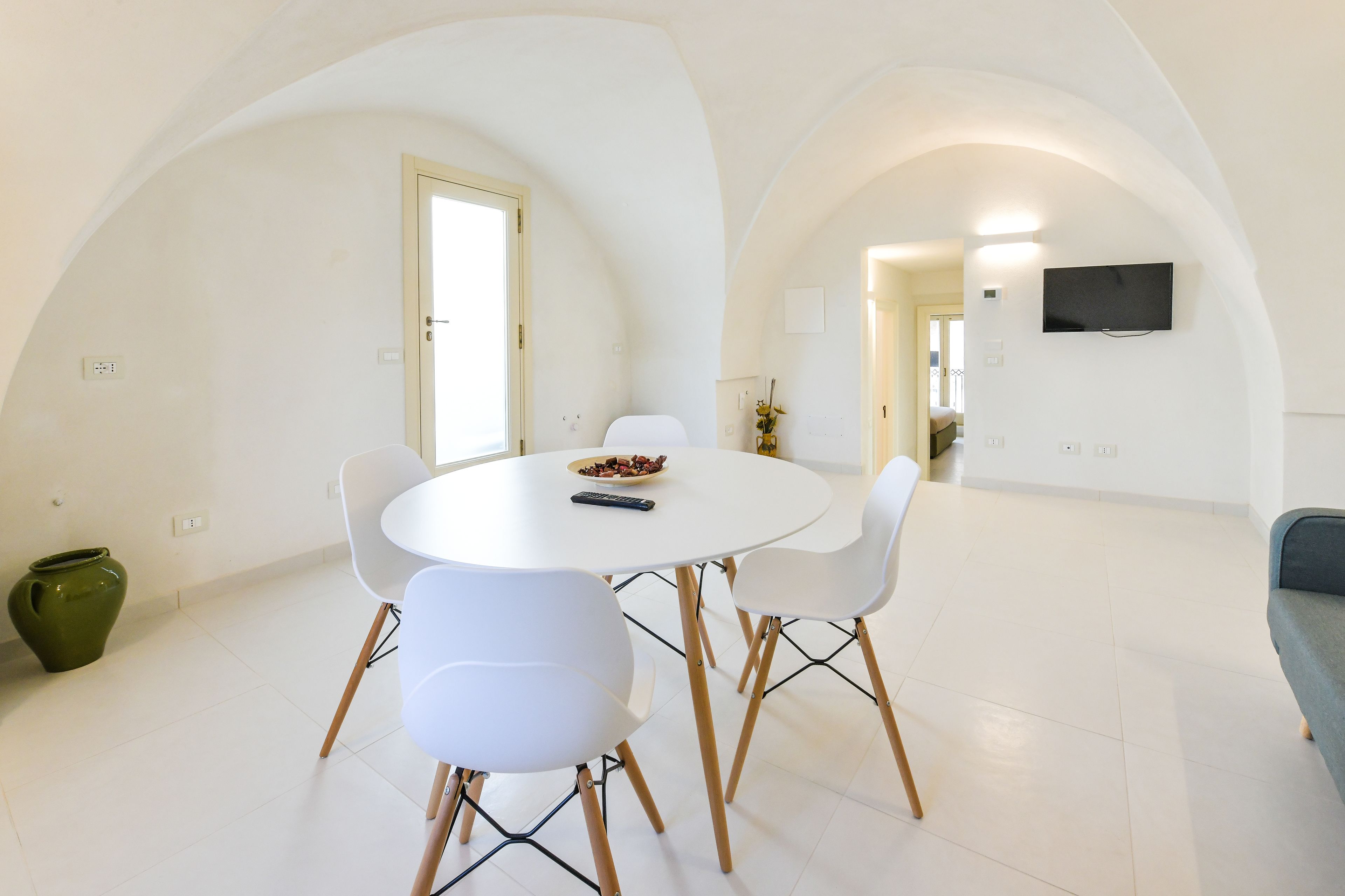 A dining area with a round table, white chairs, and a green vase.