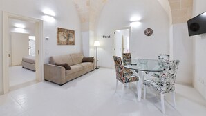 A modern living room with a sofa, a glass table, patterned chairs, a clock, and a TV. - Casa Magadè (Manduria)