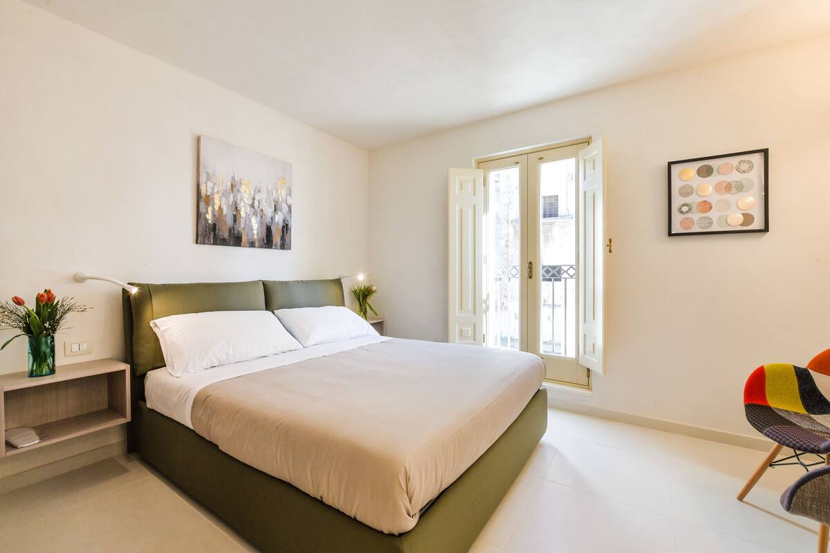 Un dormitorio moderno con una cama grande, una mesita de noche con lámpara y una silla.