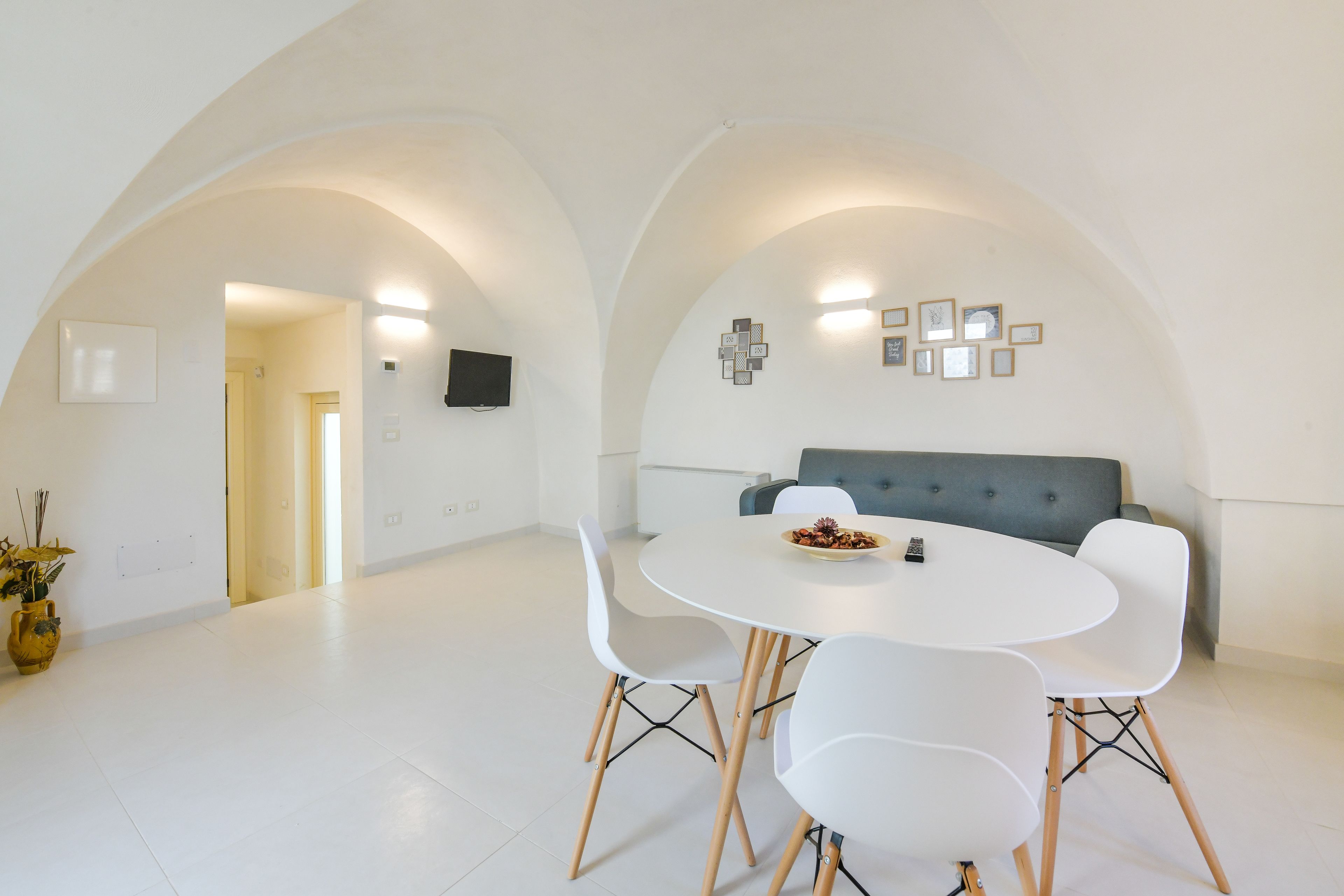 A modern dining area with a round table, white chairs, and a grey sofa.