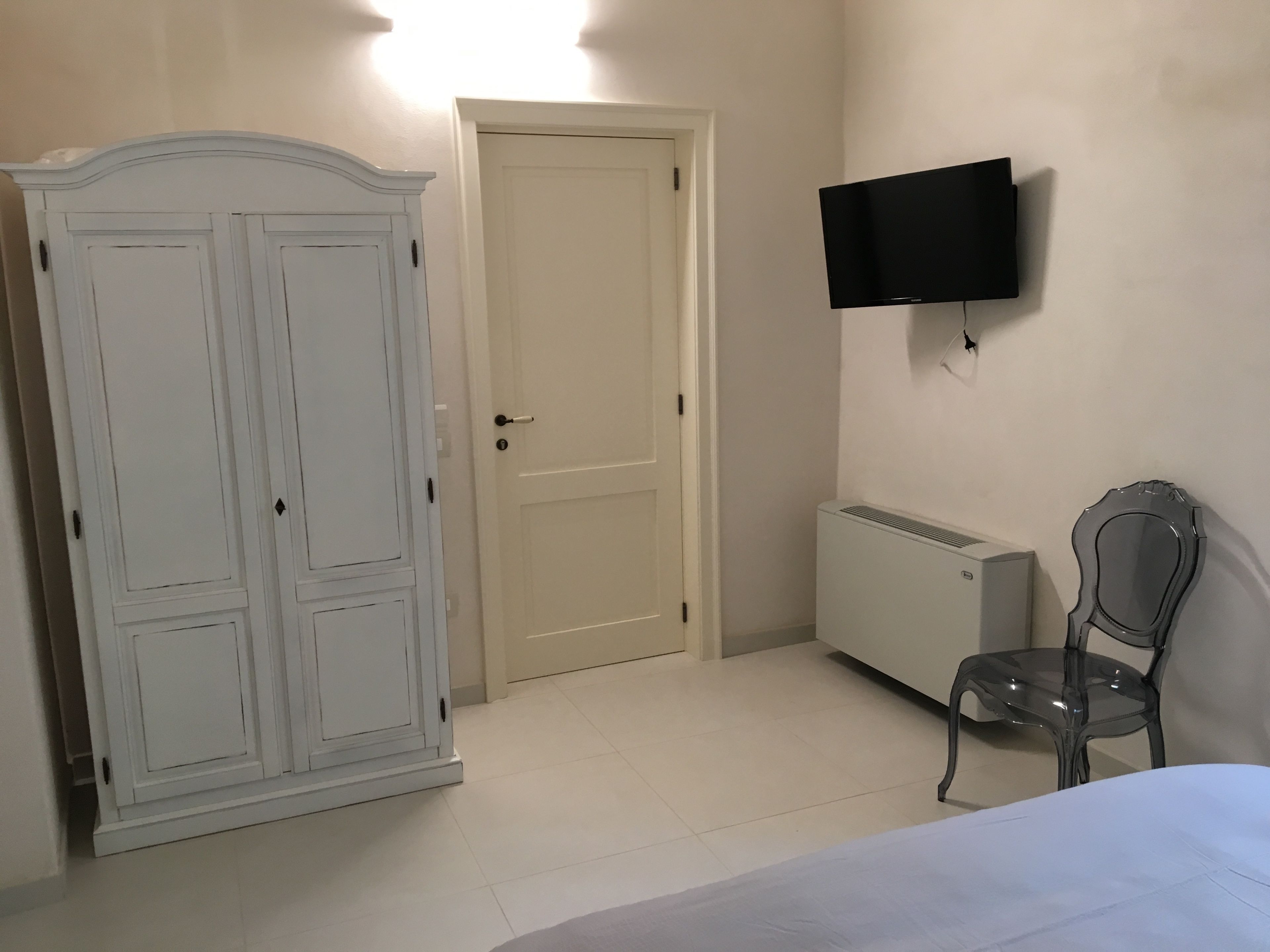 A bedroom with a bed, a wardrobe, a radiator, a chair, and a TV mounted on the wall.
