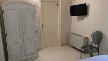Ett sovrum med en säng, en garderob, ett element, en stol och en tv som är monterad på väggen.