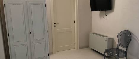 Une chambre à coucher comprenant un lit, une armoire, un radiateur, une chaise et un téléviseur fixé au mur.