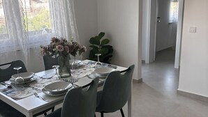 A dining area with a table set for four, a vase of flowers, and a view of a garden through a window with lace curtains.