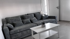 A modern living room with a grey sofa, a white coffee table, and a potted plant.