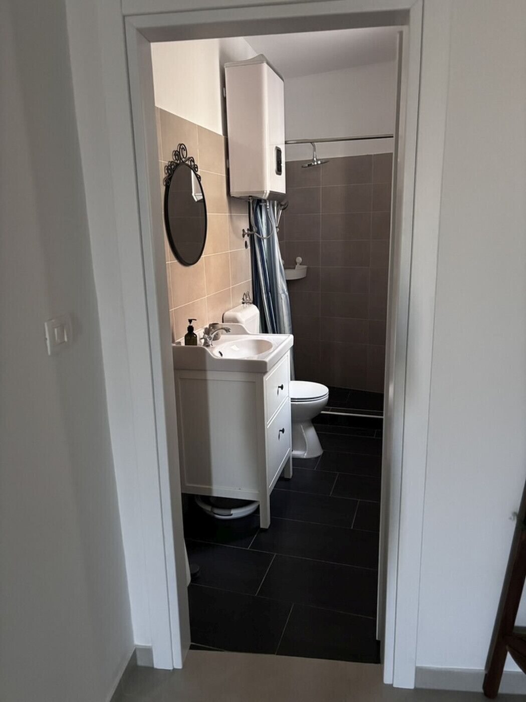 Un baño pequeño con lavamanos, inodoro y zona de ducha blancos.