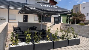 An outdoor seating area with tables and chairs, a covered umbrella, and planters with plants.